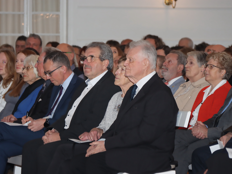 Eine Gruppe von Menschen sitzt in einem festlichen Raum und hört aufmerksam zu.