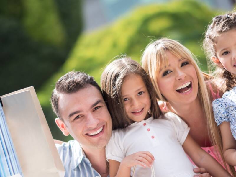 Eine fröhliche Familie trägt Einkaufstüten und lächelt in die Kamera.