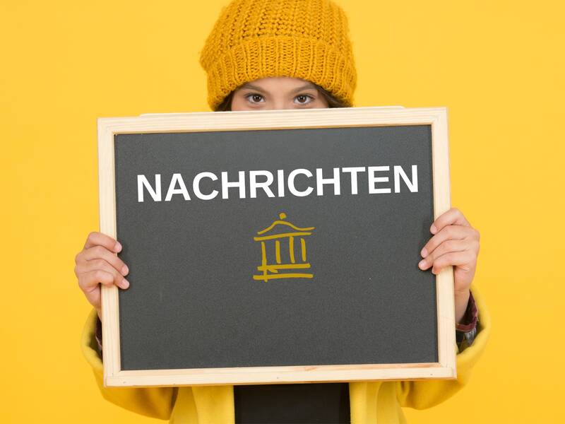 Eine Person mit gelber Mütze hält eine Tafel mit der Aufschrift "Nachrichten" vor einem gelben Hintergrund hoch.