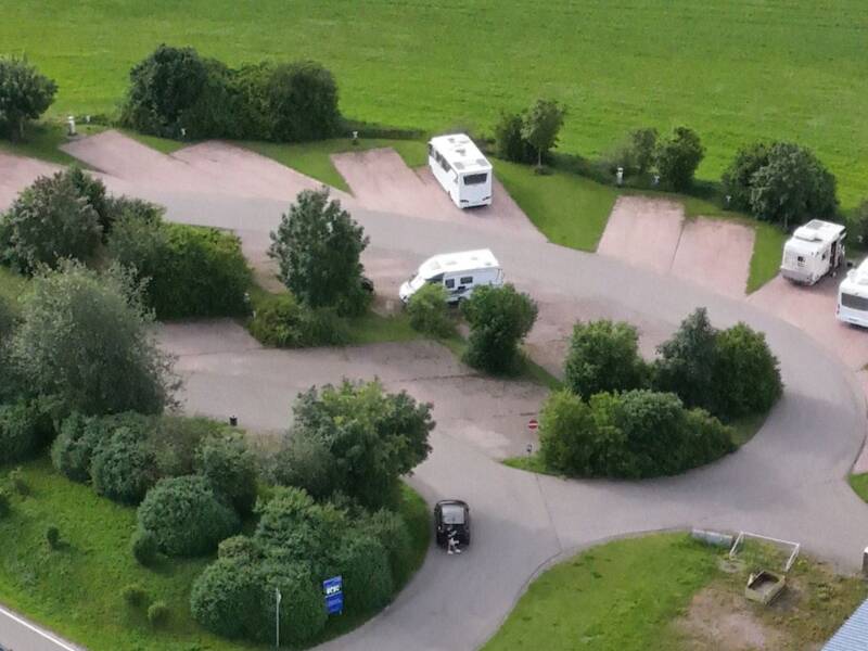 Eine Stellplatz für Reisemobile eingebettet in einer grünen Landschaft, davor verläuft eine kleine Straße