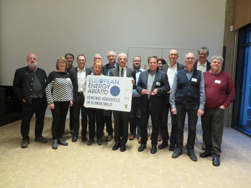 Eine Gruppe von Menschen steht in einem Raum und hält ein Schild mit der Aufschrift "European Energy Award - Gemeinde Königsfeld im Schwarzwald".