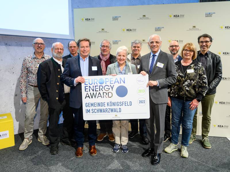 Eine Gruppe von Menschen steht vor einer Wand und hält ein Schild mit der Aufschrift "European Energy Award - Gemeinde Königsfeld im Schwarzwald".