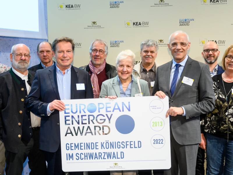 Eine Gruppe von Menschen steht vor einer Wand und hält ein Schild mit der Aufschrift "European Energy Award - Gemeinde Königsfeld im Schwarzwald".