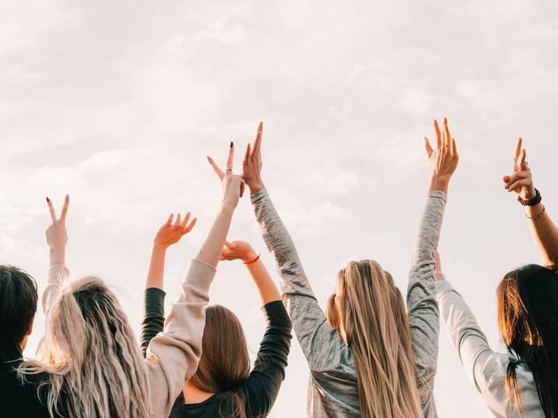 Eine Gruppe von Menschen streckt vor einem hellen Himmel die Hände nach oben und bildet mit den Fingern das Zeichen für Frieden oder Sieg.