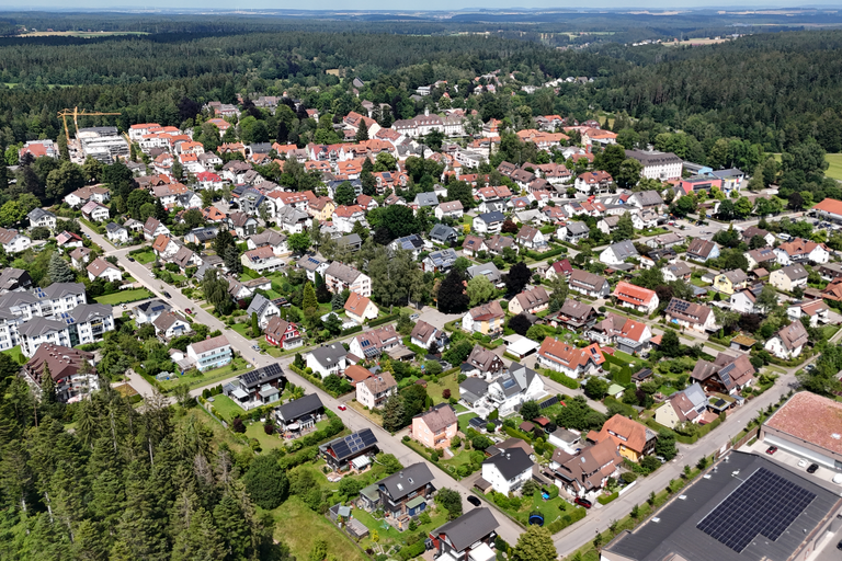 Luftaufnahme einer grünen Wohngegend mit vielen dicht beieinander stehenden Häusern, umgeben von Waldflächen.