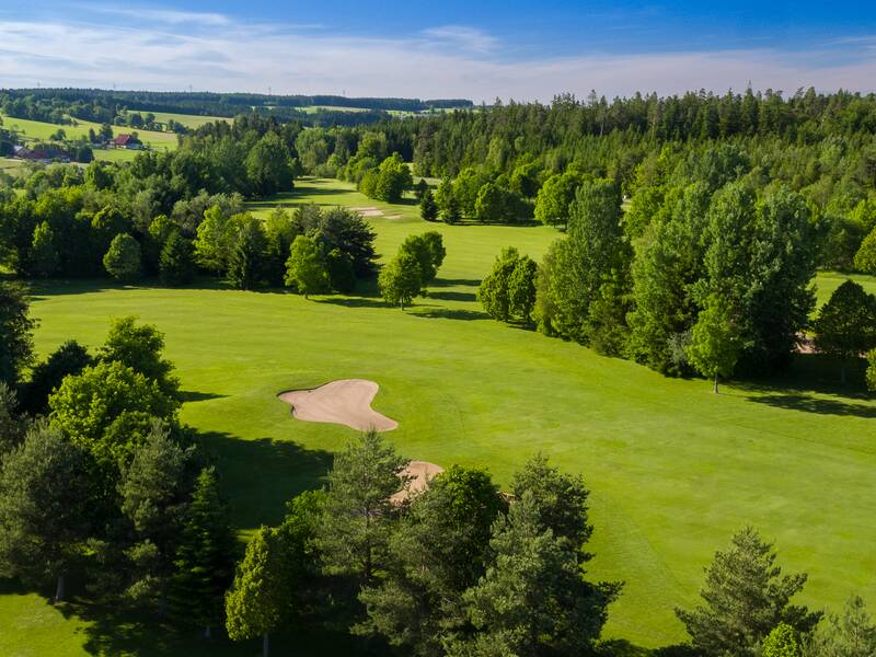 Luftaufnahme eines Golfplatzes mit üppigem grünem Rasen, mehreren Sandbunkern und umgeben von dichtem Wald.